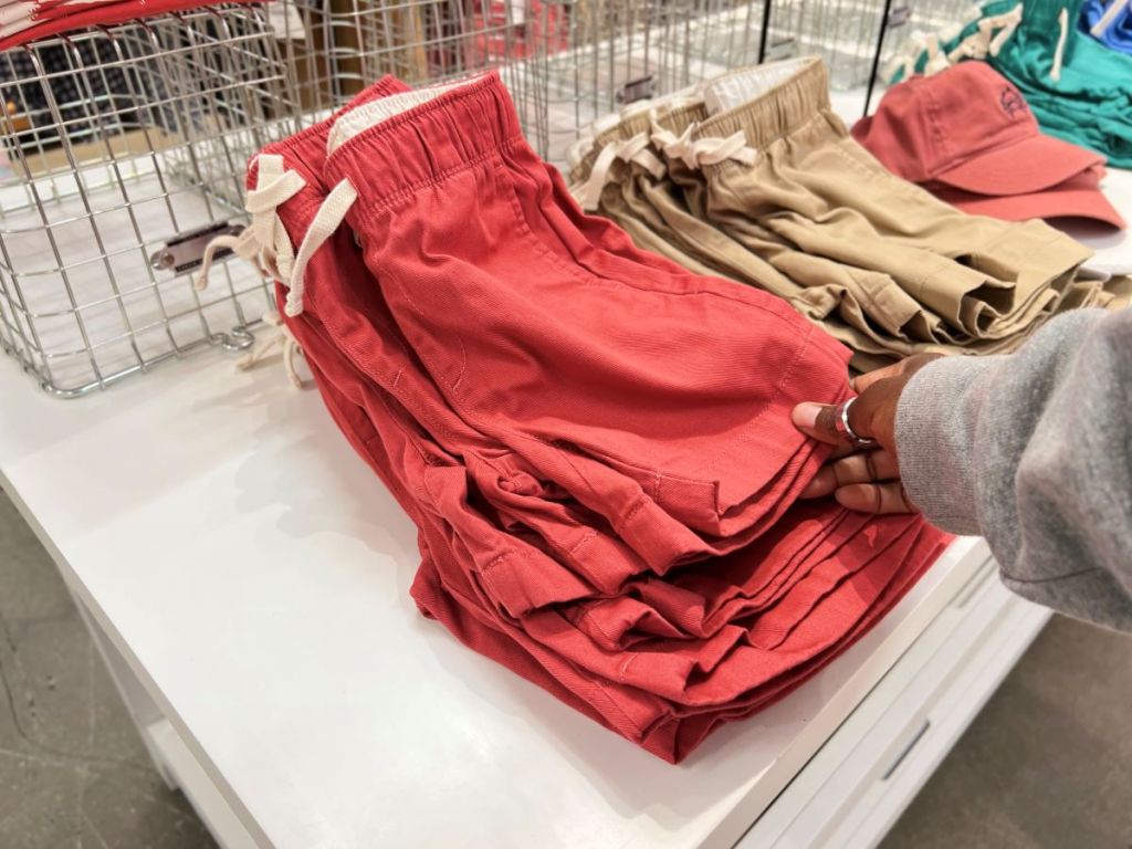 Hand holding a pair of shorts that are folded on a table at a store