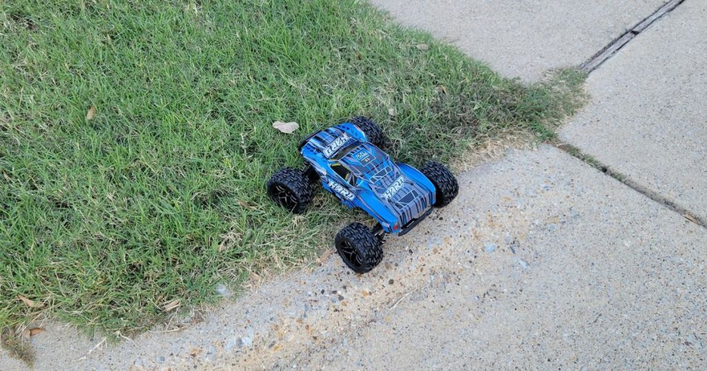 blue RC truck on grass next to sidewalk