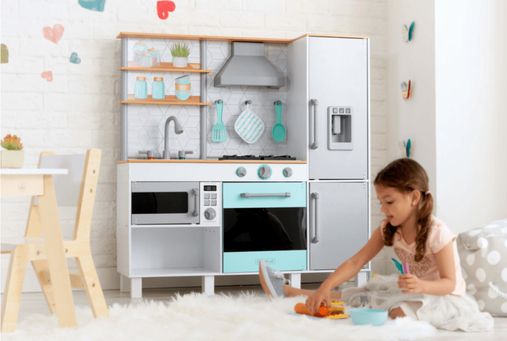a little girl playing with a Kidkraft Gourmet Kitchen Playset from Walmart