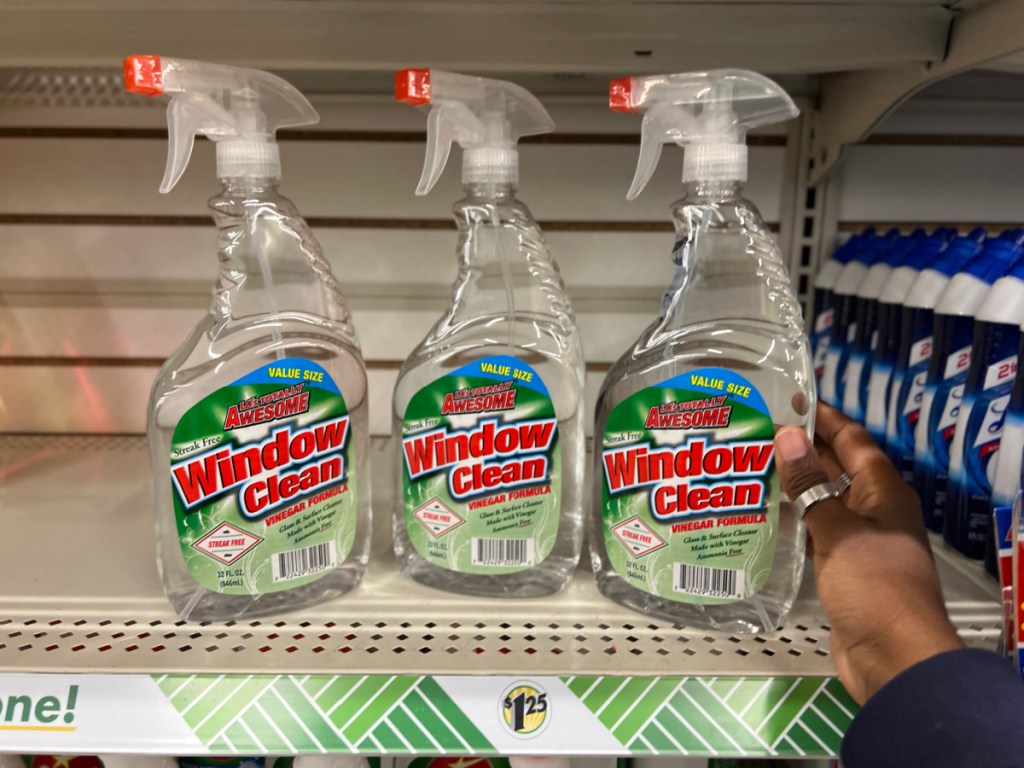 a hand grabbing LA's Totally Awesome window cleaner off the Dollar Tree shelf