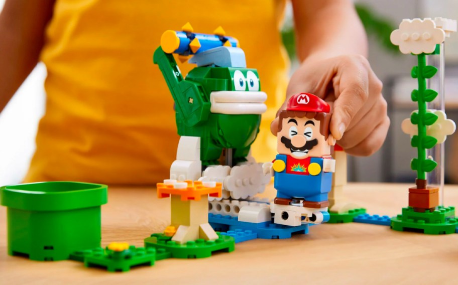 A child holding Mario playing with a LEGO Super Mario Big Spike’s Cloudtop Challenge set