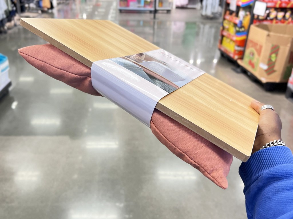 hand holding a wood lap desk with a pink cushion on the bottom