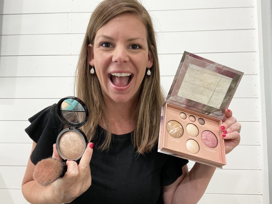 woman holding up laura geller palette, powder foundation, and brush