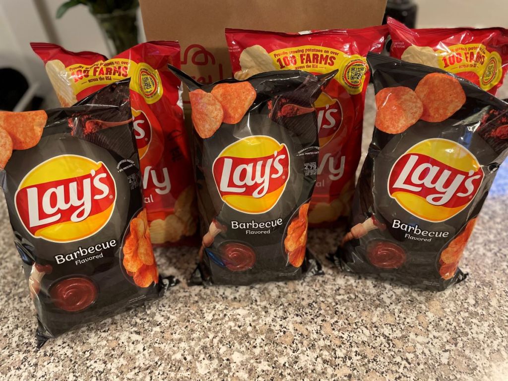 Six bags of Lay's Wavy and BBQ Chips next to a brown paper bag