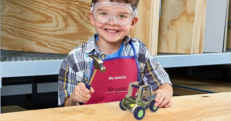 boy holding car wearing lowes kids workshop apron