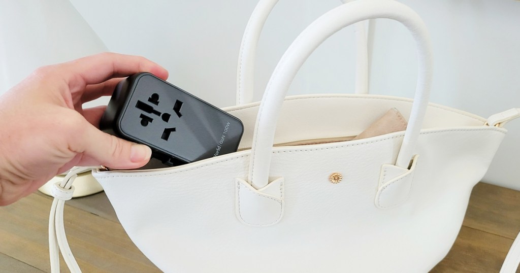 hand placing a travel adapter into a white purse