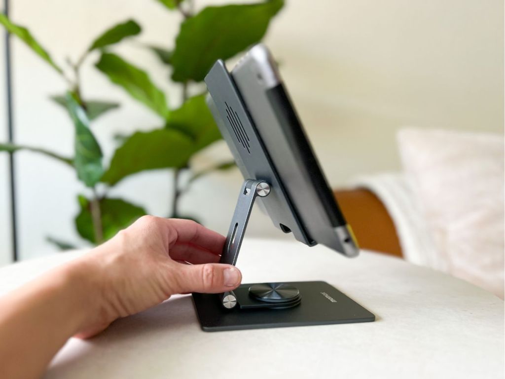 side view of hand touching ipad stand with ipad in holder placed on white table
