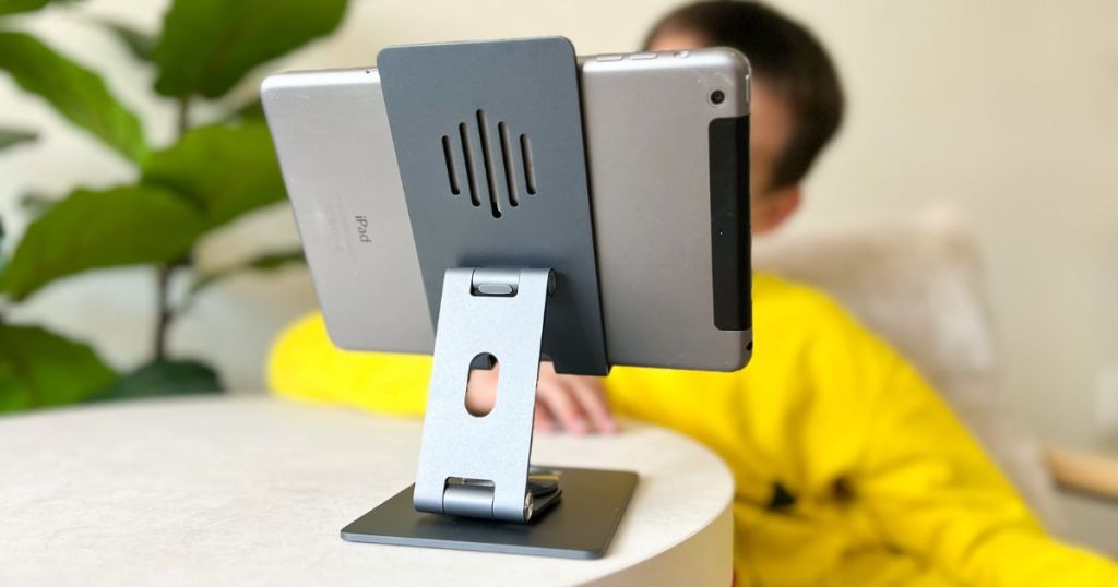 ipad stand with ipad in holder placed on white table with boy in yellow shirt watching ipad