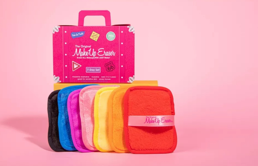 Seven makeup erasers in a row with a box that looks like a suitcase sitting on top