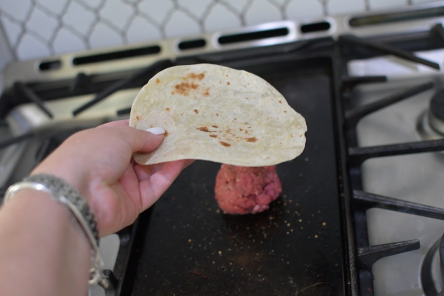 making smash burger tacos on blackstone griddle using a tortilla and beef