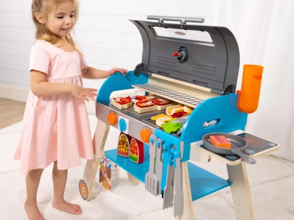 Girl standing next to a wooden grill playset