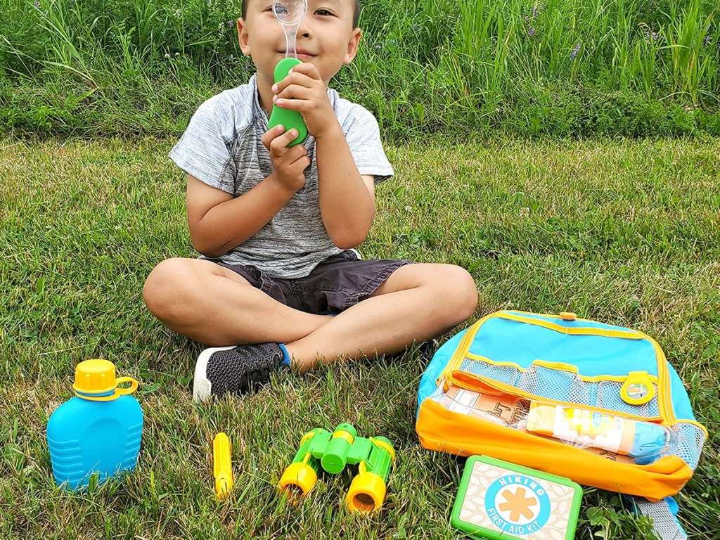 boy sitting in grass with hiking toy set