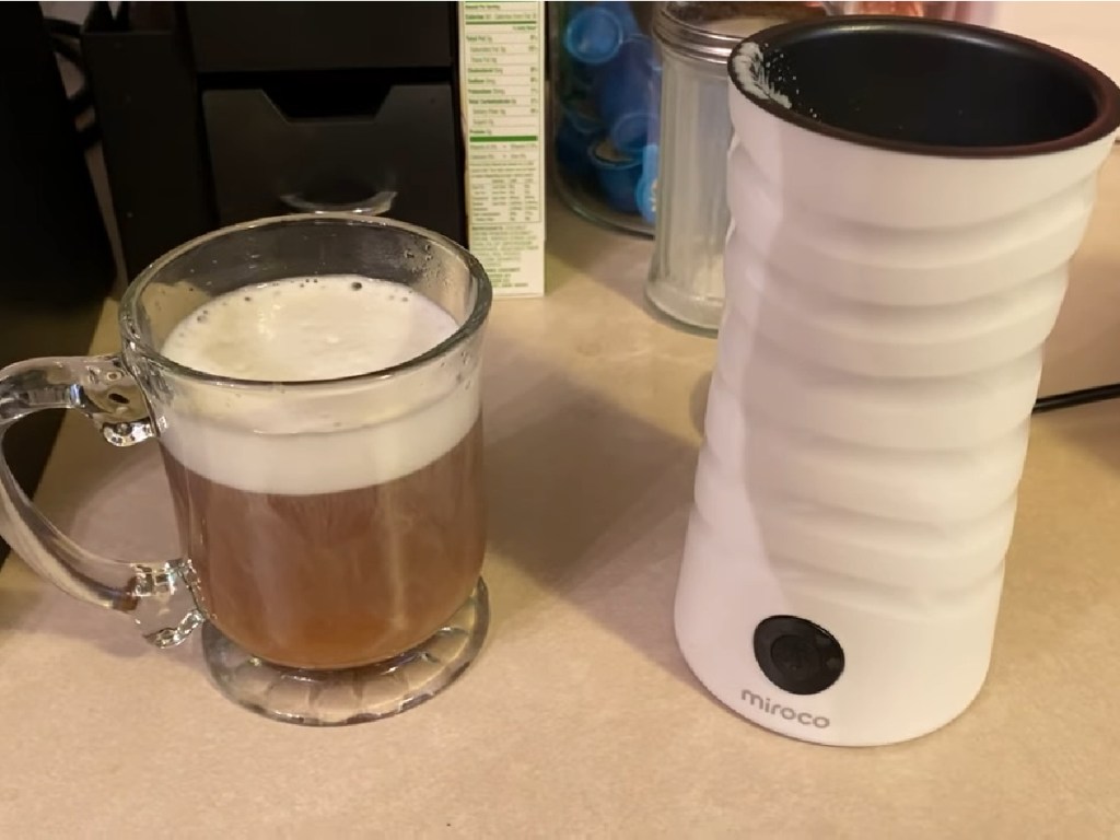 Miroco Electric Milk Frother in white next to coffee with foam on top