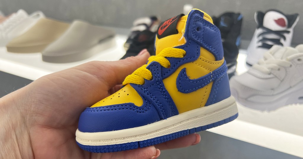 hand holding a yellow and blue nike baby shoe