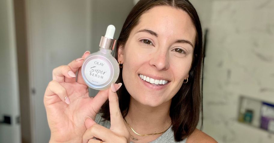 woman holding and pointing to a bottle of Olay super serum next to her face