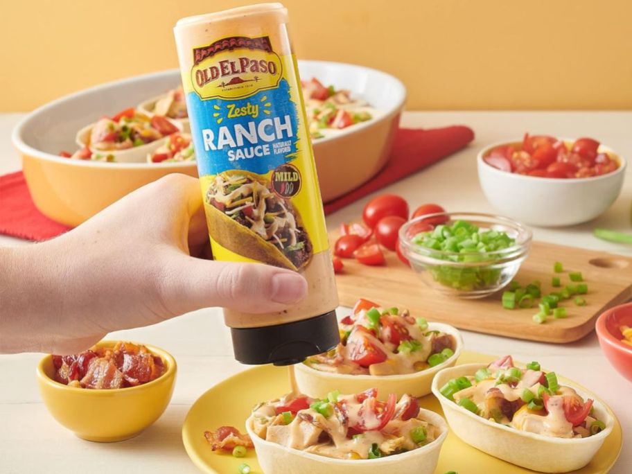 A person squeezing a bottle of Old El Paso Ranch Sauce Mild on a taco bowl