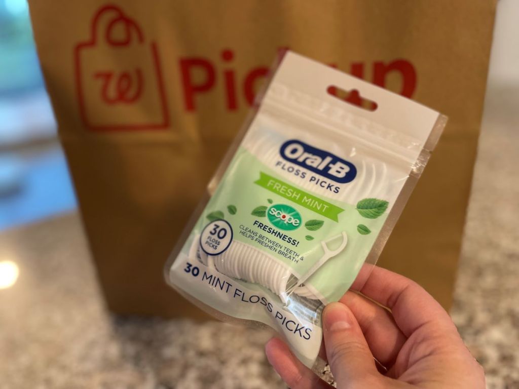Hand holding a bag of Oral-B Floss picks by a Walgreens bag