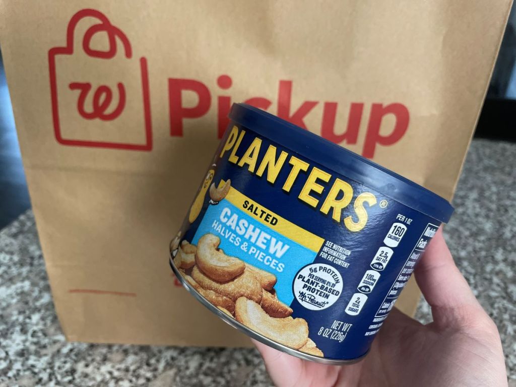 Hand holding a can of Planters cashews next to a Walgreens bag