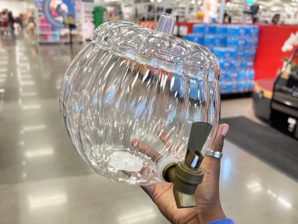 hand holding up a clear plastic pumpkin shaped beverage dispenser