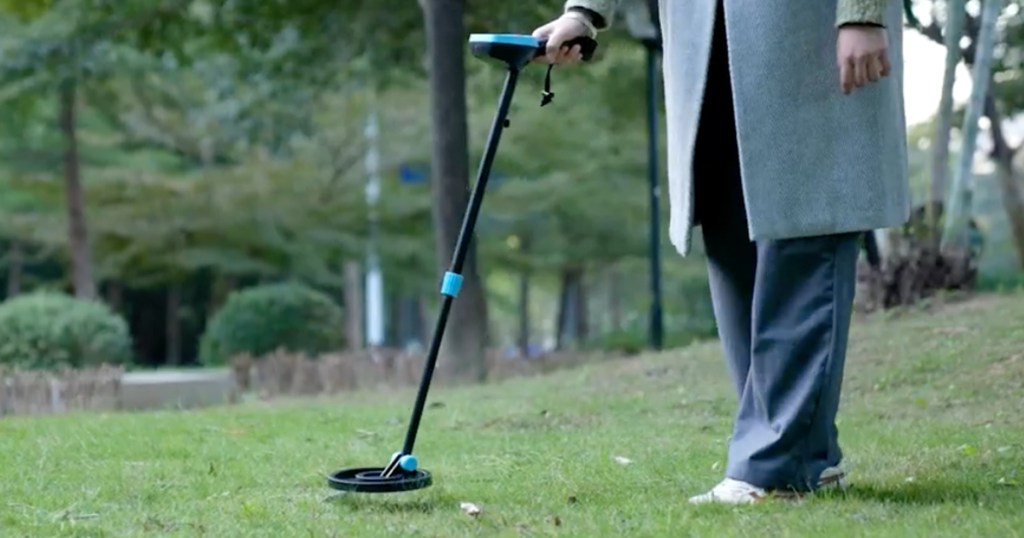 Person, die einen schwarzen und blauen Metalldetektor im Gras verwendet