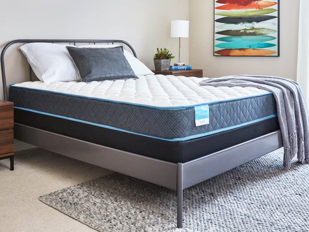 mattress on a metal bed frame with throw blanket on top