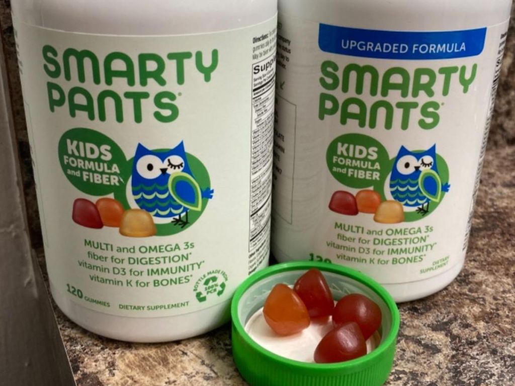 Two bottles of SmartyPants fiber gummies with a lid sent in front containing several gummy vitamins
