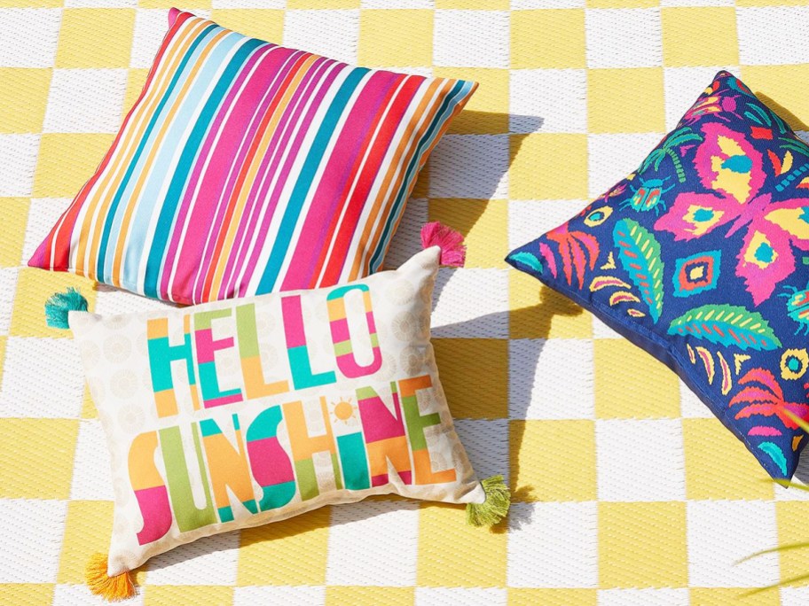 3 brightly colored outdoor throw pillows on a white and yellow checkered outdoor rug