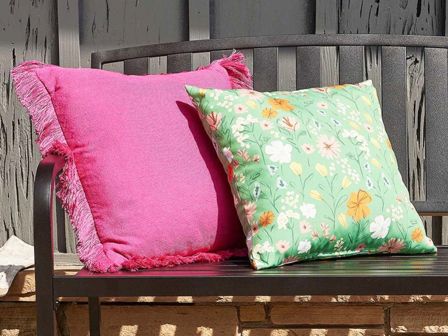 pink fringe and green floral print throw pillows on black metal bench