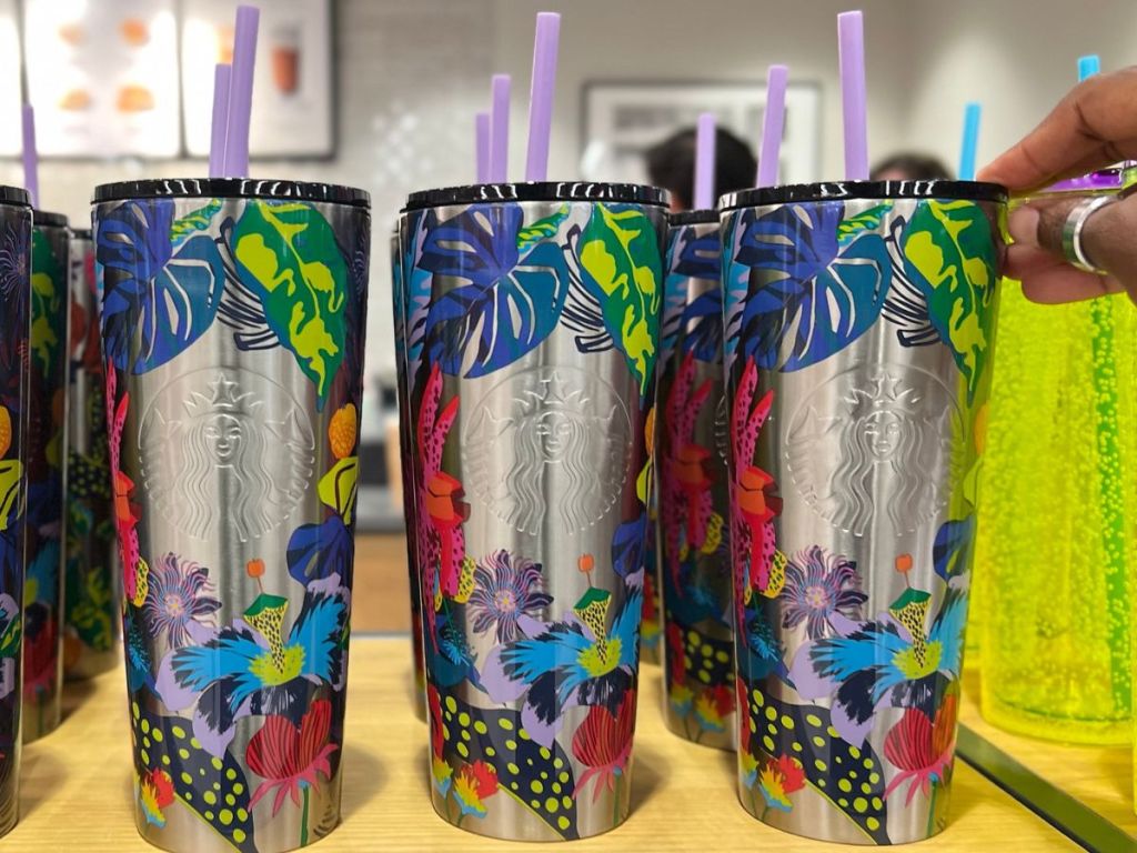 Starbucks New Immersive Florals Cold Cups on Shelf with a hand touching the top of one
