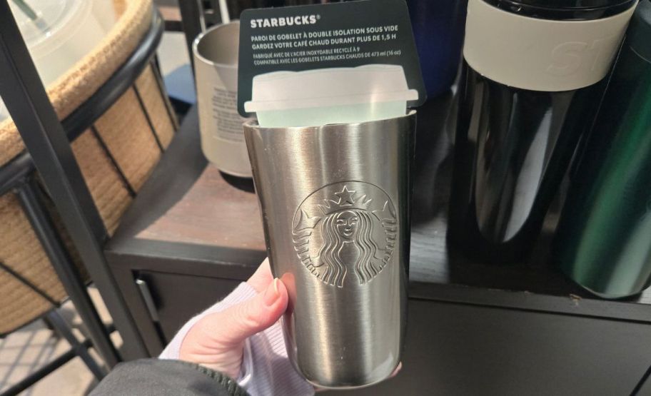 a womans hand holding a stainless steel coffee cup sleeve