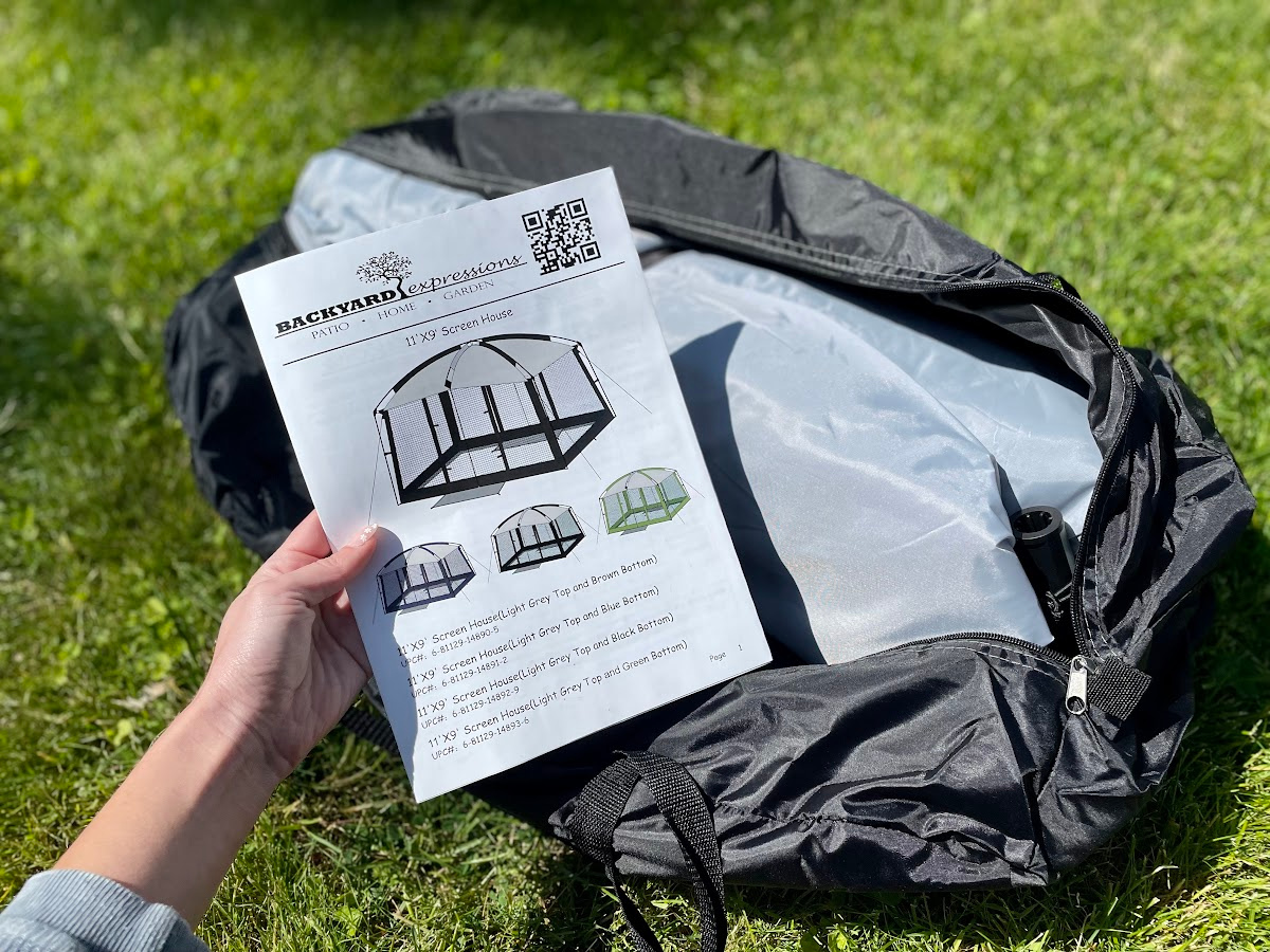 hand holding the instruction booklet for the Backyard Essentials Screened In Gazebo Tent