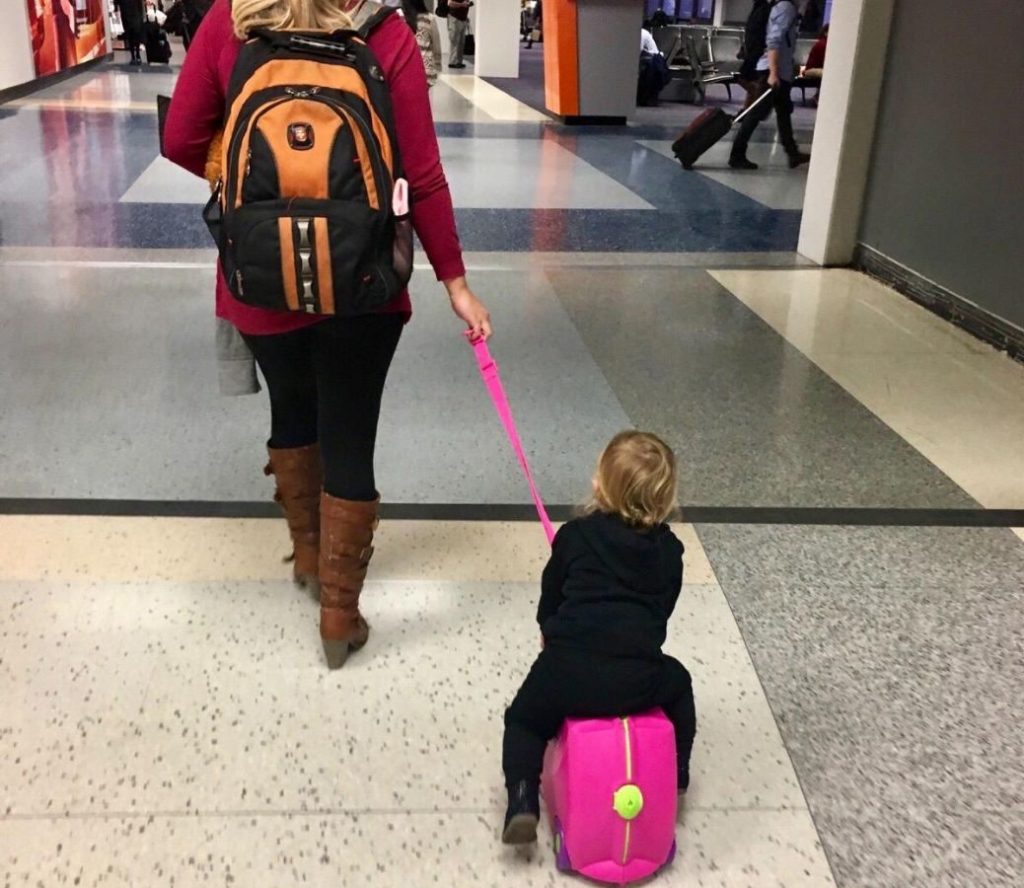 Mom toting a small child thats riding on a Trunki through an airport