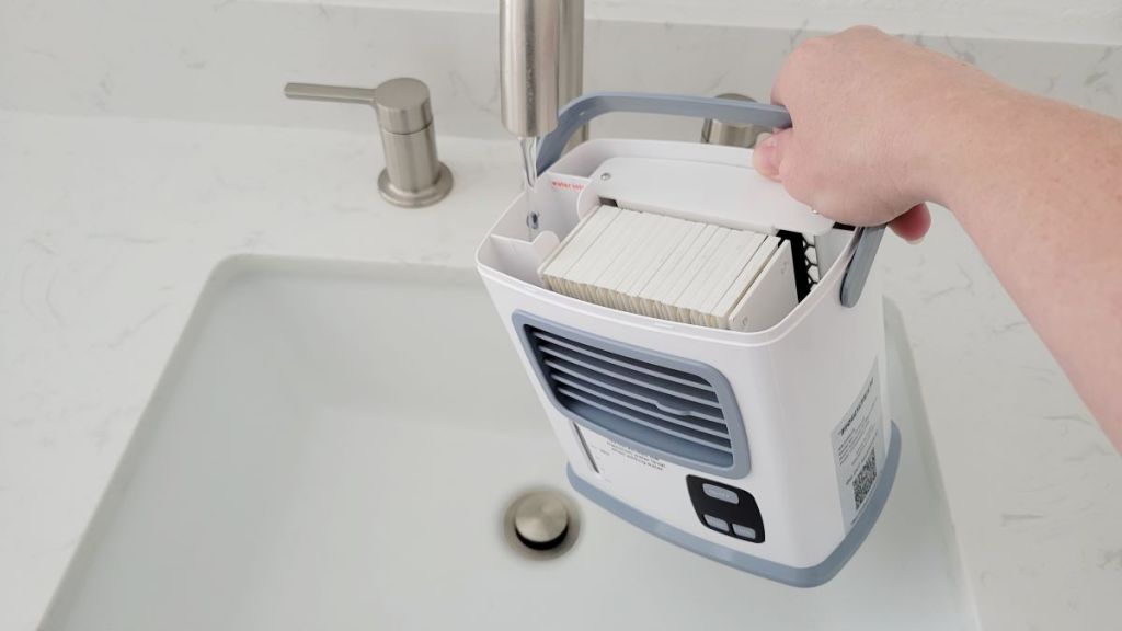 Hand holding a portable air conditioner under the faucet