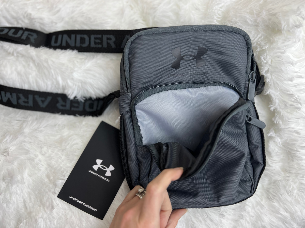 Hand holding open the front pocket of an Under Armour Louden Crossbody Bag