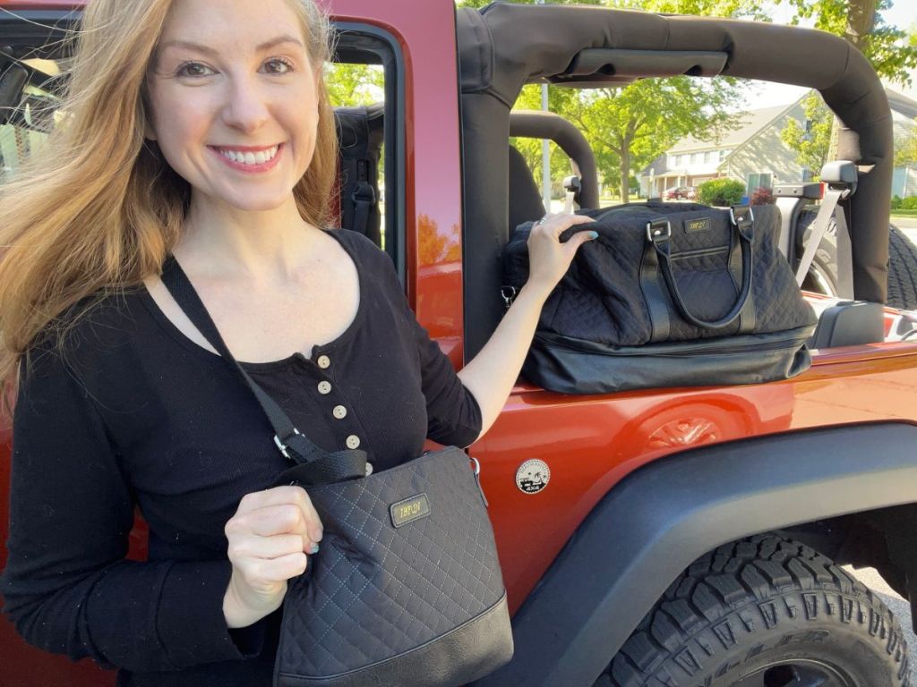 woman with UBfun weekender bag set wearing the crossbody bag while standing in front of a jeep with the weekender set on it in the background