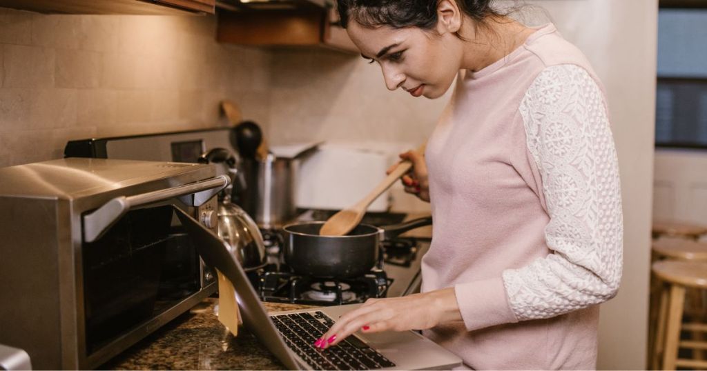Woman cooking on a stove while using a laptop