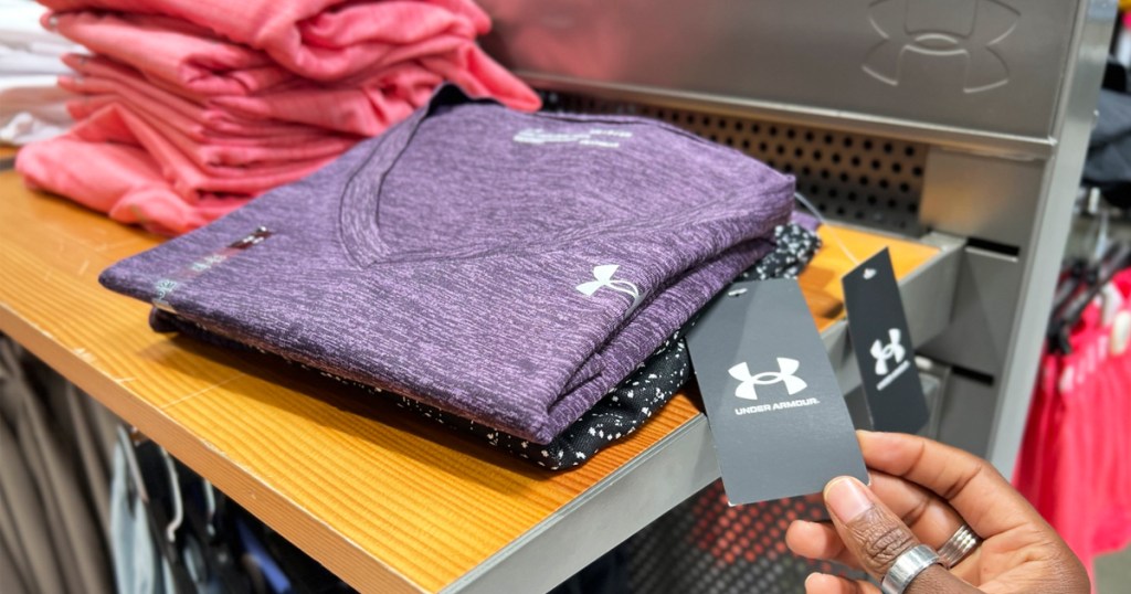 hand holding tag on a purple under armour shirt on store display shelf