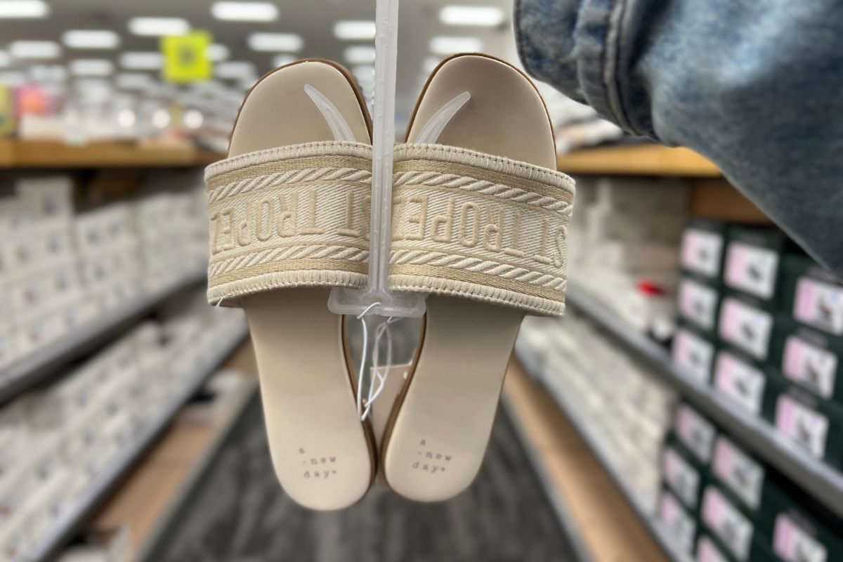 a womans hand displaying a pair of a new day st tropez/beige slides in a target store