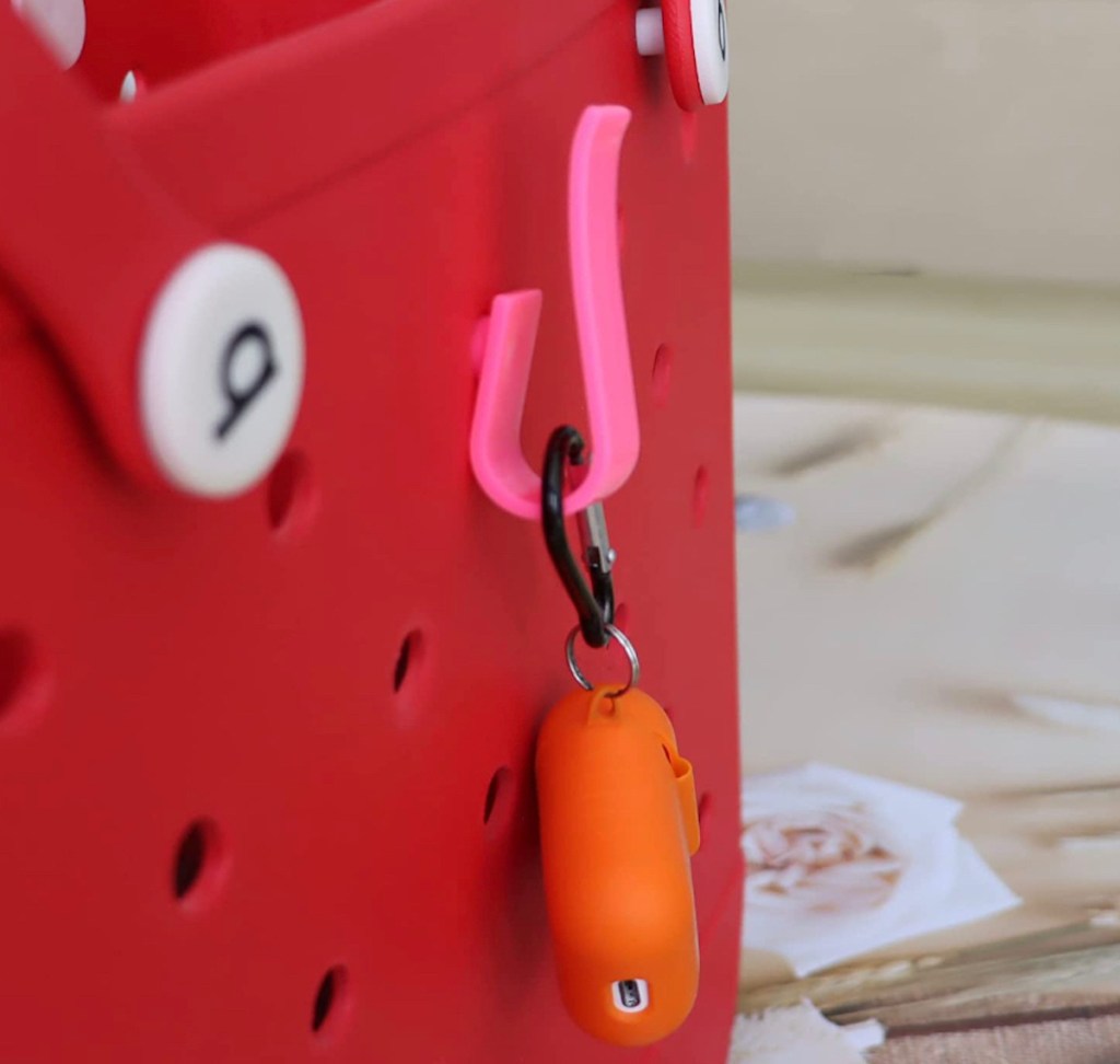 pink hook hanging from red bogg bag with orange airpods 