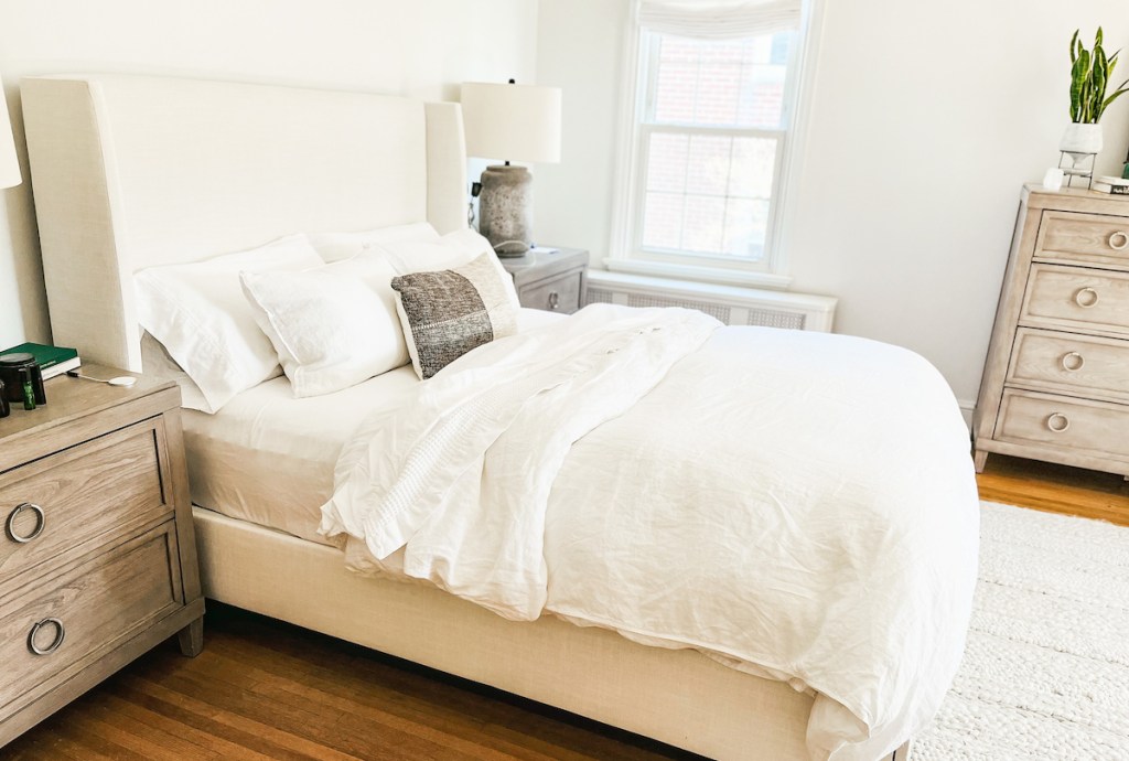 master bedroom with white bedding and beige upholstered headboard