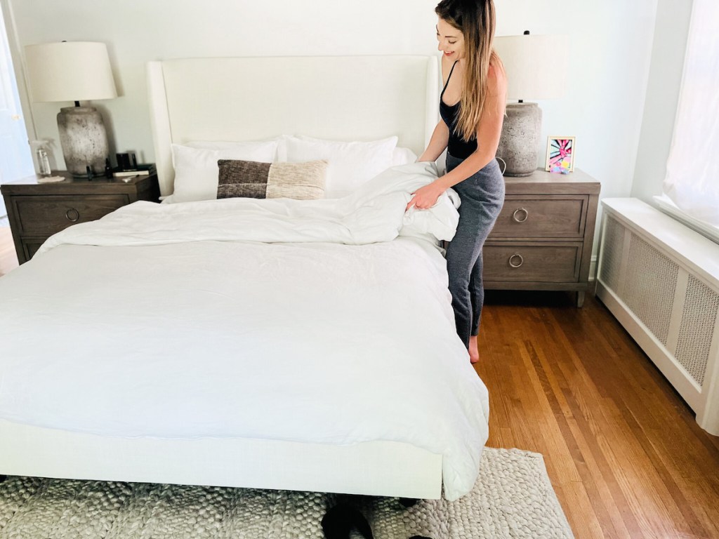 woman holding side of bedding in master bedroom