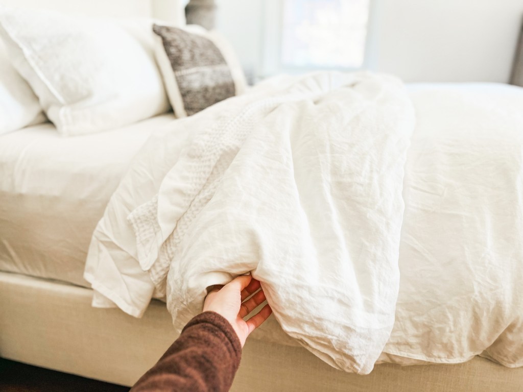 hand holding edge of white duvet and insert on how to make a bed