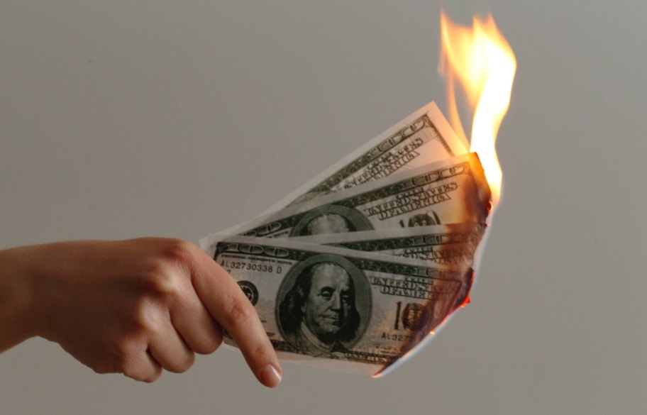hand holding hundred dollar bills catching on fire, perhaps due to tipping culture and tipping fatigue