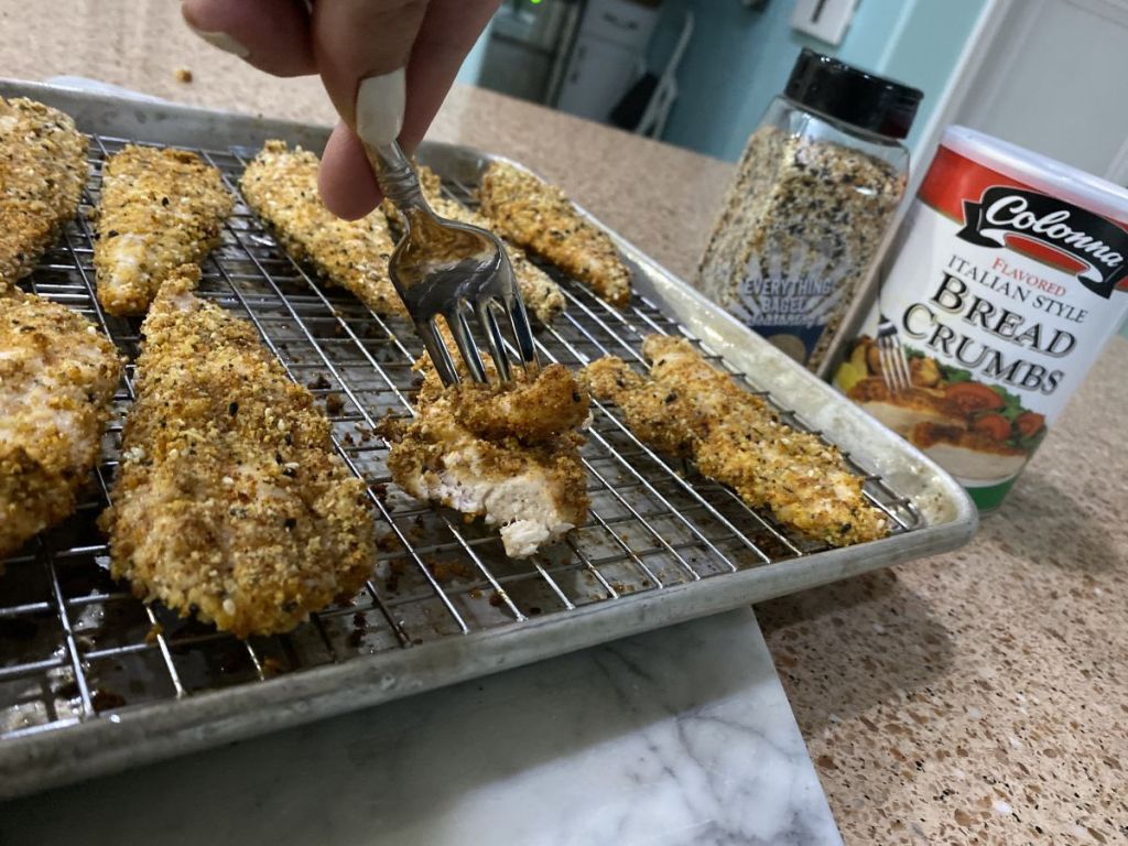 person taking fork to chicken strips on baking sheet