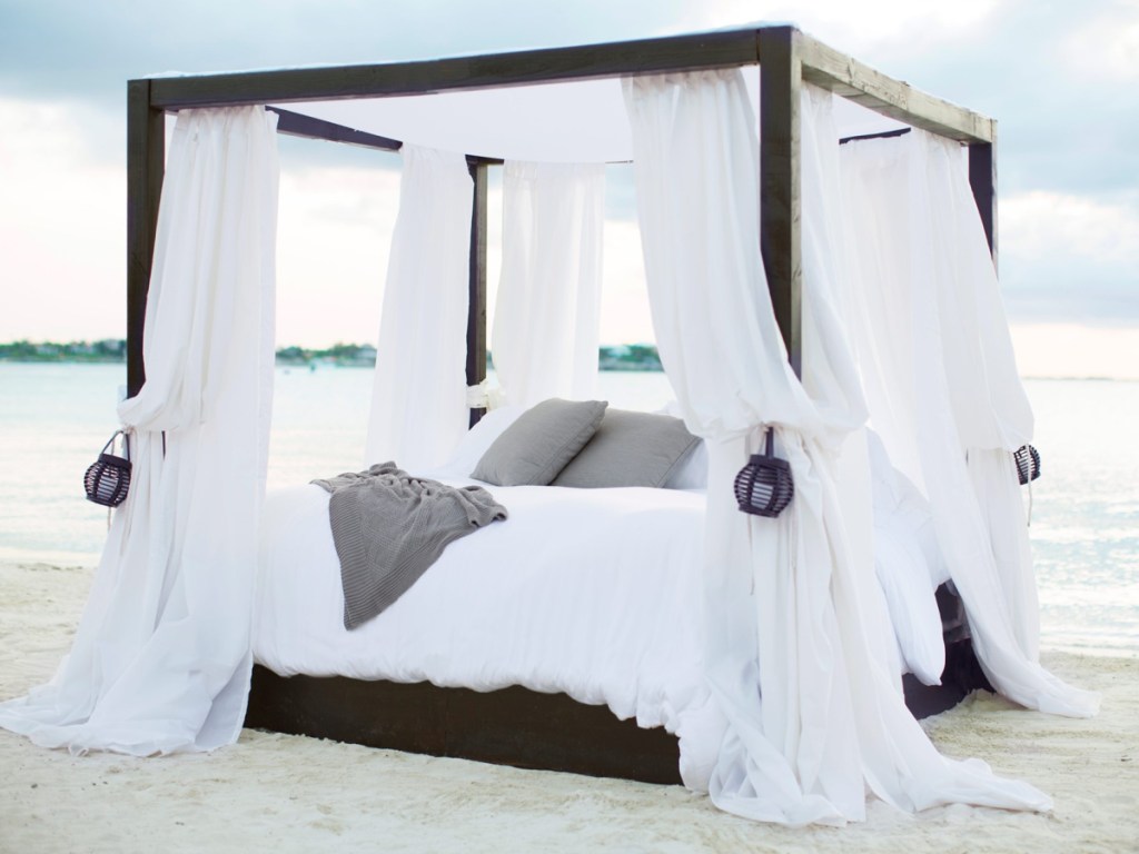 bed with white sheets and curtains on beach