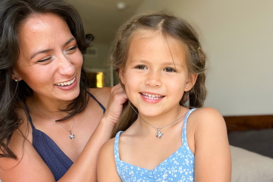 mom putting birthstone flower necklace on daughter