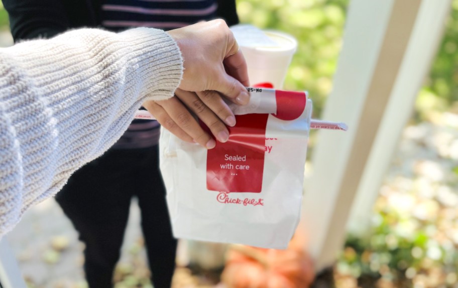 two hands holding onto chick fil a bag in doorway