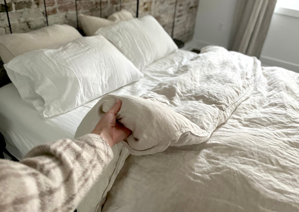 hand holding edge of linen duvet on bed
