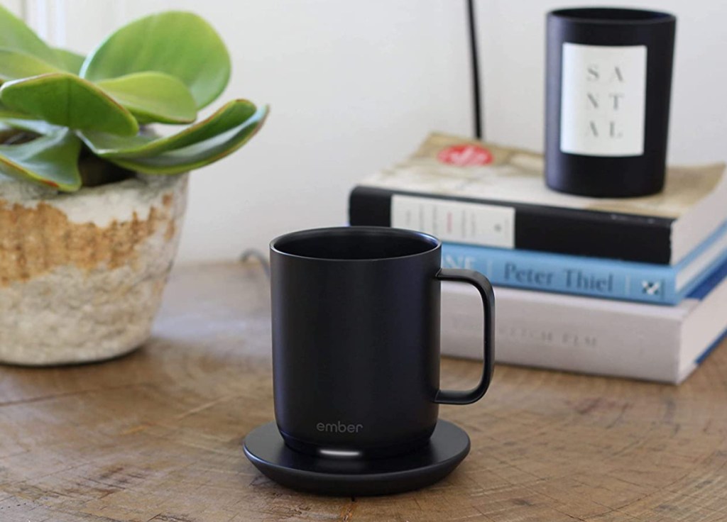 ember coffee mug on coaster in front of books and a plant