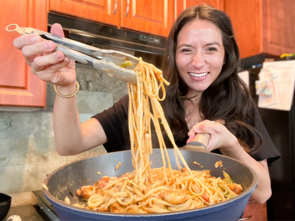 woman pulling noodles out of pan with tongs
